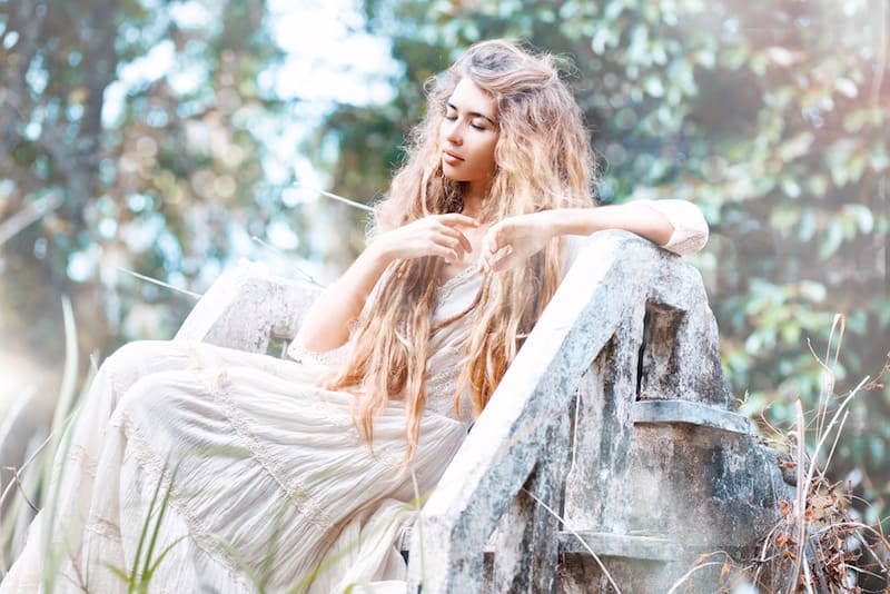 boho girl contemplating life in a white dress, sitting in a field