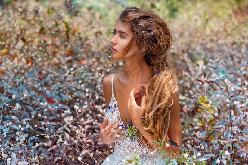 boho girl with dreadlocks in a white dress, sitting in a field