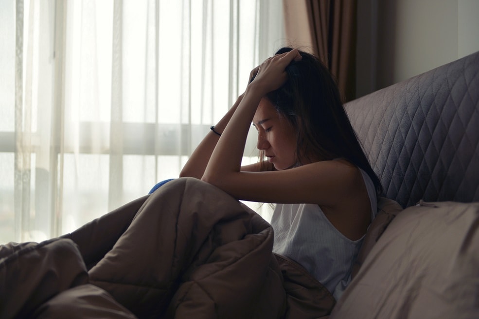 woman depressed in bed, holding her head in her hands