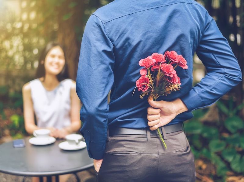 man surprising girlfriend with flowers behind his back