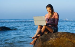 girl working on laptop on a rock at the beach