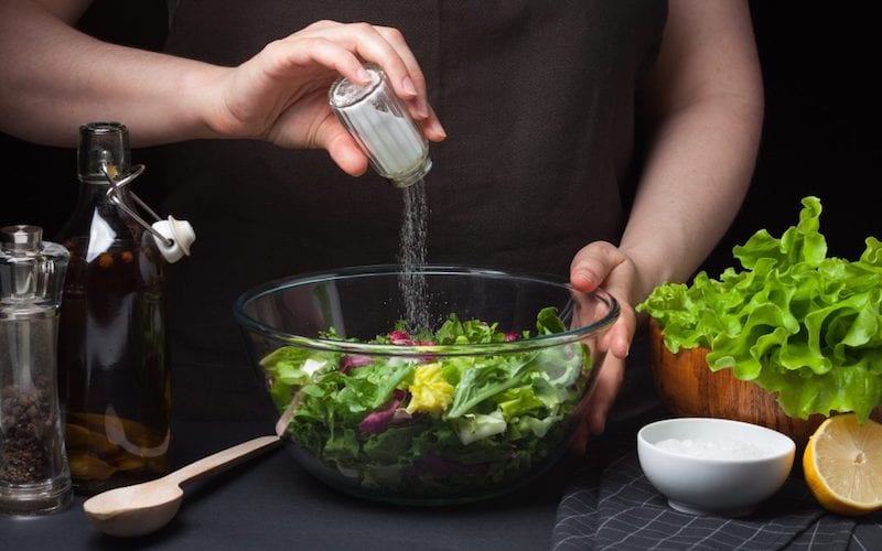 pouring salt into a raw vegan salad, seasoning, flavour