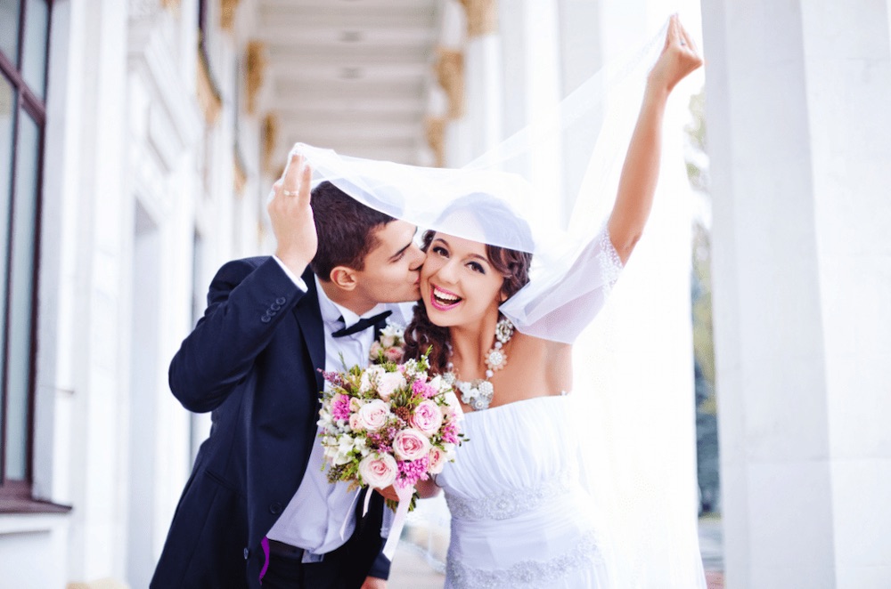 cute happy couple at their wedding, kissing underneath the brides veil