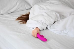 woman holding a dildo/vibrator in bed, masturbation